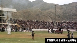 Taliban fighters and thousands of residents of the Afghan capital, Kabul, watch as surgeons cut off a thief's hand in the national stadium on August 7, 1998.