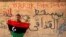 Демонстрант у Тобруку на сході Лівії тримає старий «дореволюційний» прапор країни часів монархії, яку скинув переворот Каддафі. На стіні написи: «Тобрук сьогодні вільний», «Геть Каддафі!»