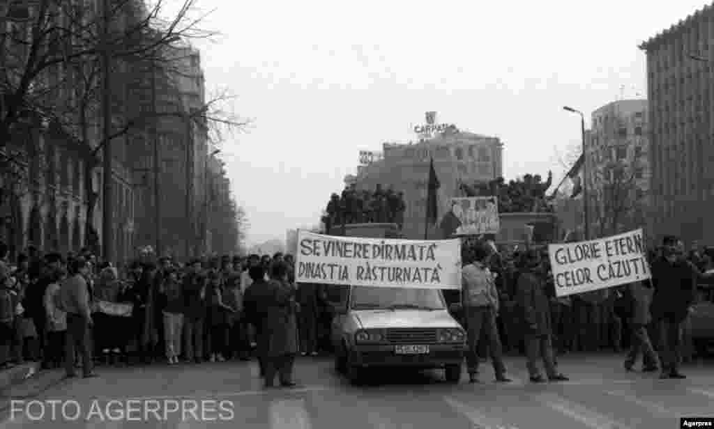 București, 22 decembrie1989. Manifestanți fericiți pe bdul Magheru. Înscrisul de pe una dintre pancarde amintește de politica dezastroasă de demolări a lui Nicolae Ceaușescu. Biserica Sf. Vineri, ridicată de moștenitoarea marii familii boierești Herescu, fusese vreme de două secole un extraordinar așezământ caritabil. Sf. Vineri era pentru bucureșteni un loc emblematic. La fel și Spitalul Brâncovenesc ridicat de o altă boieroaică, Safta Brâncoveanu, care donase pentru ridicarea și întreținerea lui 8 moșii. Demolarea unor astfel de simboluri a dat naștere la zeci de legende urbane care explică până astăzi în fel și chip moartea violentă a lui Nicolae Ceaușescu&nbsp;