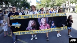 Oamenii țin un banner pe care scrie „Niciun tratat de pace fără întoarcerea copiilor ucraineni deportați” în timpul unui miting de susținere a Ucrainei, organizat cu ocazia Zilei Independenței Ucrainei, la Paris, pe 24 august 2025.