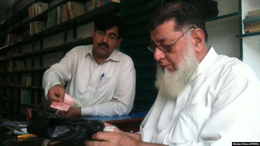 Haji Rasheed (right) bags a book for a customer in front of the dwindling stock of books at his Maktaba-e Sarhad bookstore in Peshawar.