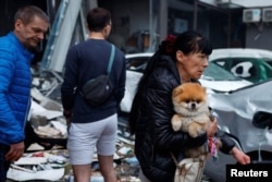 Žena nosi psa kod stambene zgrade oštećene u ruskom napadu raketama i dronovima u Kijevu 6. jula.