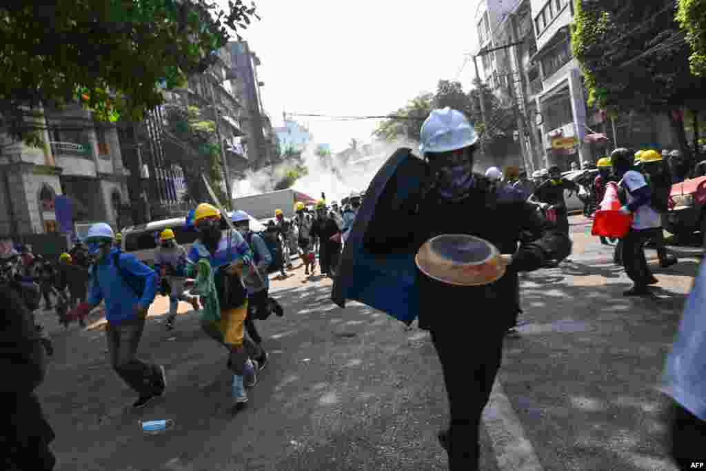 Protesters run away from tear gas from riot police during a demonstration against the military coup, in Yangon on March 2, 2021.