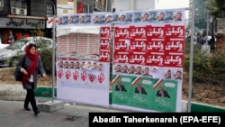 An Iranian woman walks past electoral posters on a street in Tehran.