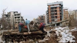 Câțiva copii se joacă pe un tanc avariat în fața unei clădiri distruse din cartierul Kovacici din Sarajevo, în februarie 1996.