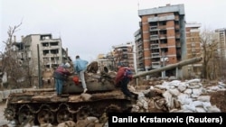 Câțiva copii se joacă pe un tanc avariat în fața unei clădiri distruse din cartierul Kovacici din Sarajevo, în februarie 1996.