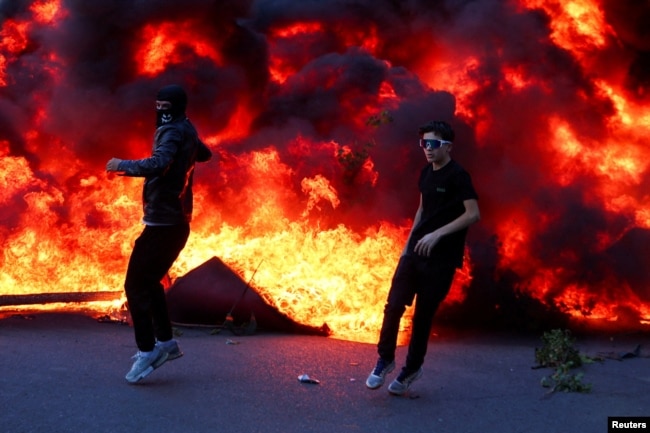 Dy protestues para një zjarri të madh gjatë protestës në Tiranë, Shqipëri, 14 tetor.
