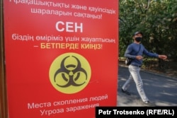 Мужчина проходит мимо плаката, сообщающего об опасности коронавируса, на улице Алматы