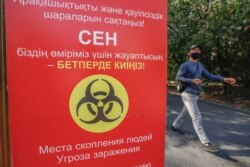 Маска таққан ер адам коронавирус індеті жайлы ескерту жазылған баннер жанынан өтіп барады. Алматы, 11 қыркүйек 2020 жыл.