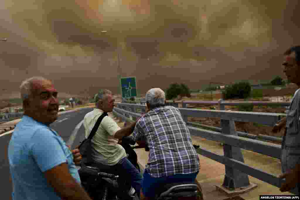 People in the Greek town of Kineta, near Athens, look at smoke as a wildfire burns on July 23. (AFP/Angelos Tzortzinis)