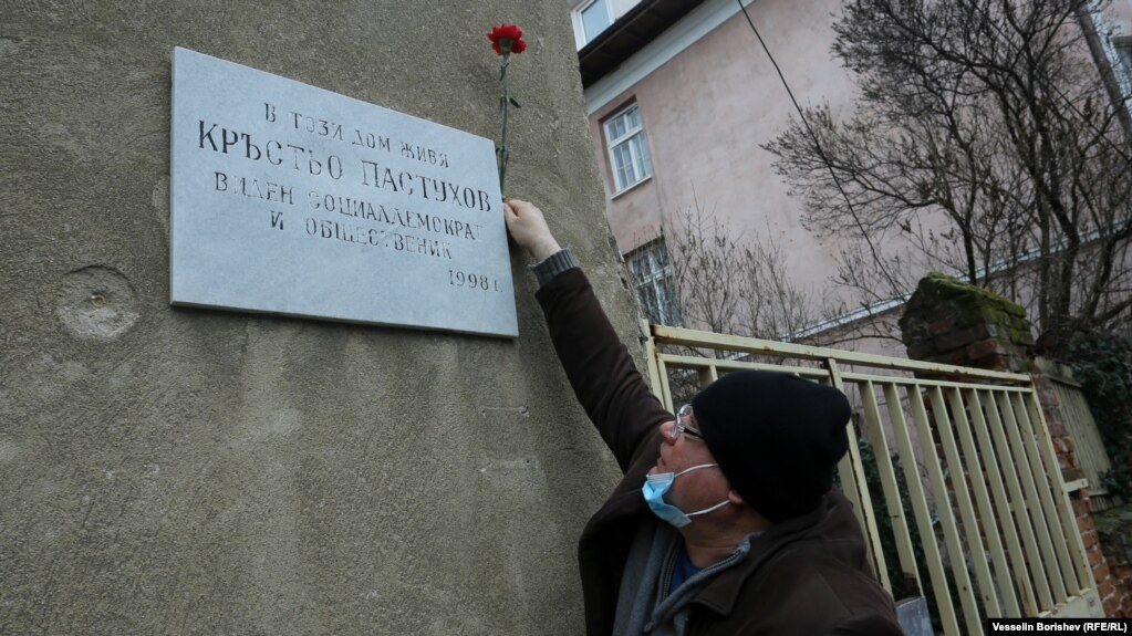 Мъж с предпазна маска закрепва цвете на паметната плоча на Кръстьо Пастухов, поставена тук през 1998 година. Адресът е ул. "Бенковски" 36. Пастухов (1874-1949) е един от лидерите на българските социалдемократи и министър на вътрешните работи и народното здраве през 1919 г. Той е противник на управлението на Борис Трети през 30-те и началото на 40-те години. След преврата на 9 септември 1944 г. той е осъден на 5 години затвор и умира като затворник на 25 август 1949 г.