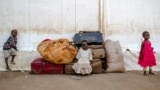 Three young children sit in front of a pile of luggage at the Renk Transit Center in Renk, South Sudan, on November 17, 2025.
