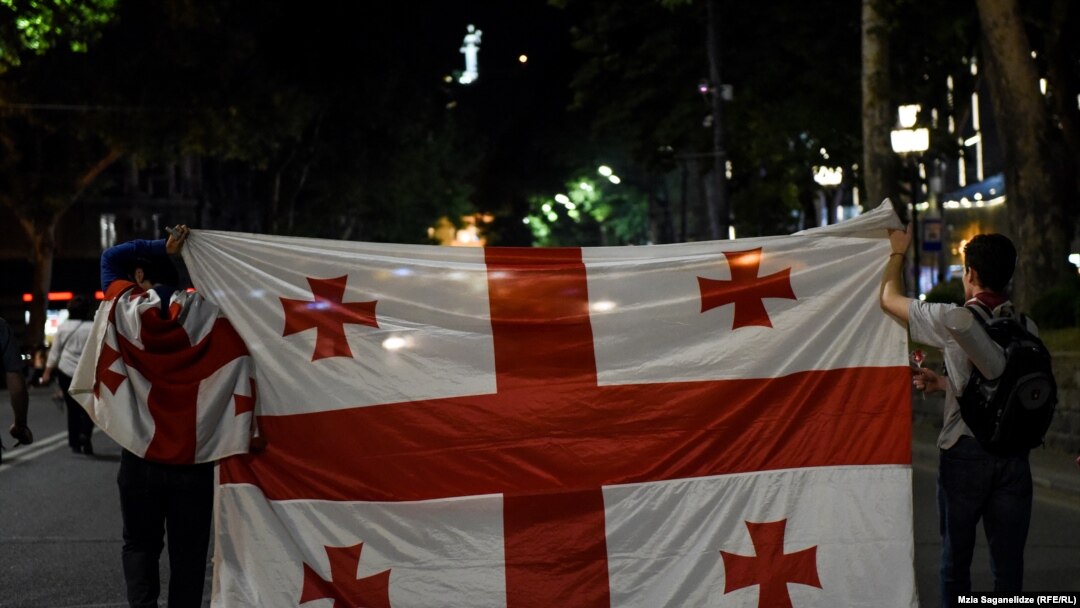 Protesters waive the Georgian flag near the parliament building in Tbilisi early on June 26.