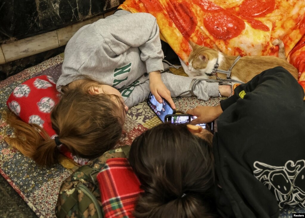 Dy banore të Kievit, të shtira në dyshemenë e metrosë, duke shikuar telefonat mobilë, më 12 korrik.
