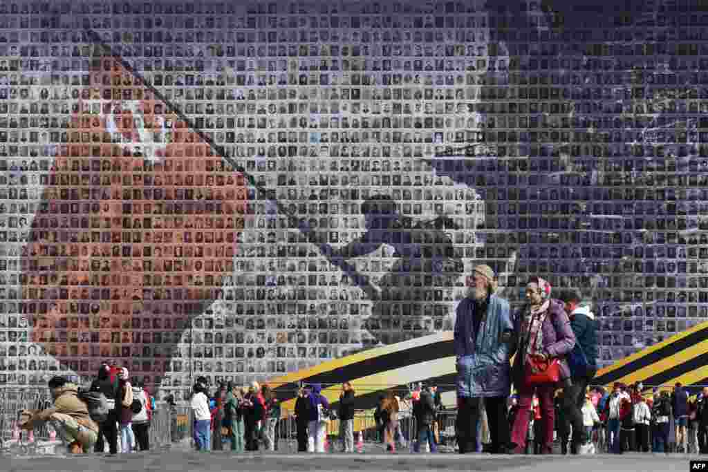 People walk past a giant banner in Saint Petersburg depicting a Red Army soldier raising the Soviet flag over the Reichstag in Berlin. The image, created from 4,500 portraits of World War II veterans, is being displayed ahead of the 80th anniversary of Victory Day on May 9, which marks the defeat of Nazi Germany.