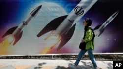 Një grua kalon pranë një posteri ku shfaqen raketat që Teherani nisi më herët gjatë javës ndaj Izraelit. Teheran, 19 prill 2024. 