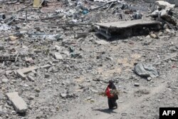 O femeie palestiniană cară câteva vreascuri, pe lângă dărâmături și moloz în cartierul al-Tuffah din orașul Gaza, pe 14 august 2025.