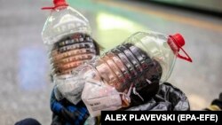 Disa djem mbajnë maska ​​mbrojtëse, doreza dhe shishe uji të modifikuara në një karrocë në një aeroport në Kinë.