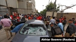 Police officers survey a damaged car at the site of an attack at the Pakistan Stock Exchange entrance in Karachi on June 29.