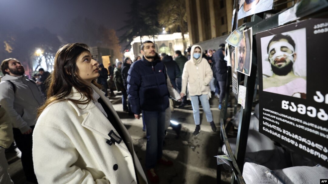 O femeie din Tbilisi se uită la un afiș care arată oameni bătuți de poliția georgiană. 9 decembrie.