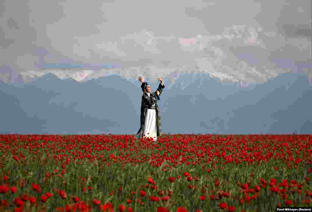 Женщина в традиционном казахском костюме позирует перед своей знакомой на поле цветущих маков у гор Тянь-Шаня в Алматинской области