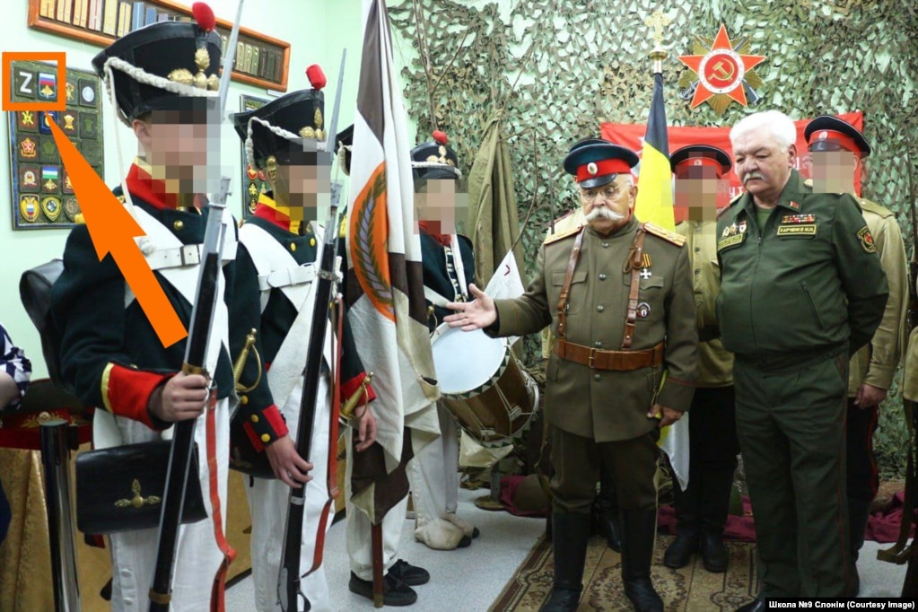 Выхаванцы «Грэнады» у форме Расейскай імпэрыі на выставе «Вайсковая атрыбутыка» ў Слонімскім краязнаўчым музэі. Разам зь імі Віктар Пенза і вайсковы пэнсіянэр Міхаіл Харчанка. На сьцяне шаўроны расейскай арміі зь літарай Z, дзеці трымаюць расейскі чорна-жоўта-белы імпэрскі сьцяг.