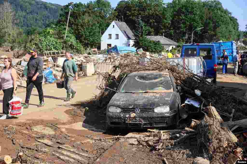 Люди проходят мимо поврежденного автомобиля после наводнения в Зинциге, Германия, 18 июля 2021 года