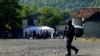 Një pjesëtar i njësive speciale të Policisë së Kosovës ecën pranë disa serbëve, që po protestojnë në Jarinjë më 26 shtator. 