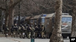 Солдати російської армії стоять біля своїх вантажівок під час мітингу проти російської окупації на площі Свободи в Херсоні, березень 2022 року