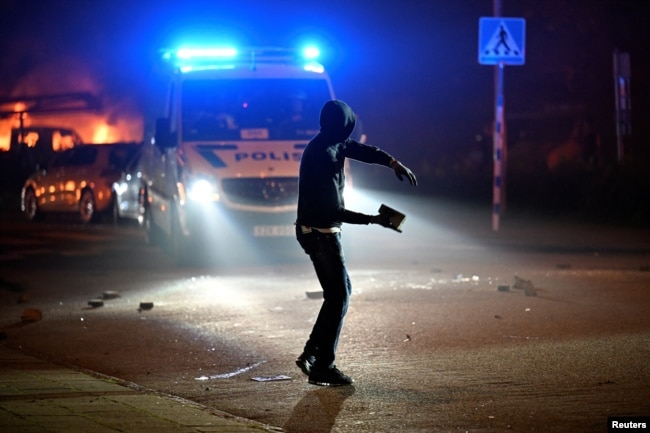 Një person duke hedhur gur në drejtim të veturës së policisë gjatë trazirave të dhunshme në Malmo, Suedi, 3 shtator 2023.