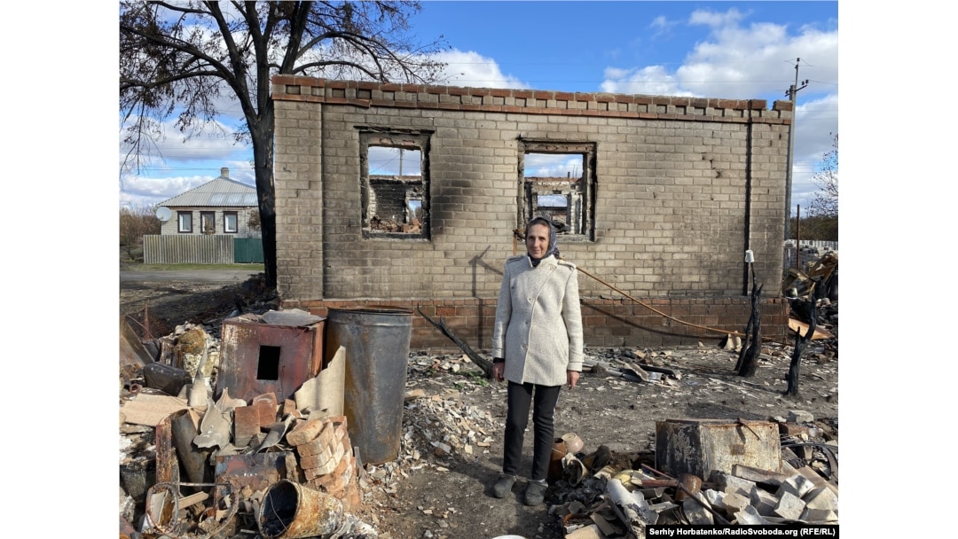 Lydia Prokopenko stands in front of the remains of her house, which was destroyed by a forest fire.