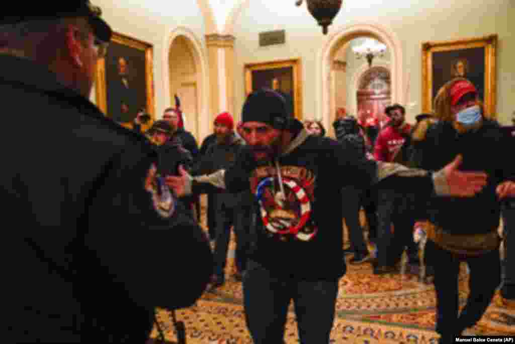Trump erőszakos támogatói a capitoliumi rendőrségnek mutogatnak az amerikai szenátusi kamara előtti folyosón.
