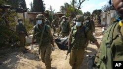 Израильские солдаты несут тело человека, убитого в результате нападения ХАМАС в кибуце Кфар-Азза во вторник, 10 октября 2023 года