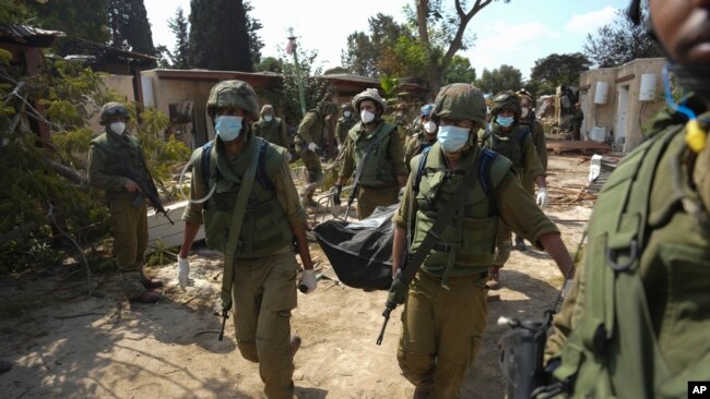 Израильские солдаты несут тело человека, убитого в результате нападения ХАМАСА в кибуце Кфар-Азза во вторник, 10 октября 2023 года