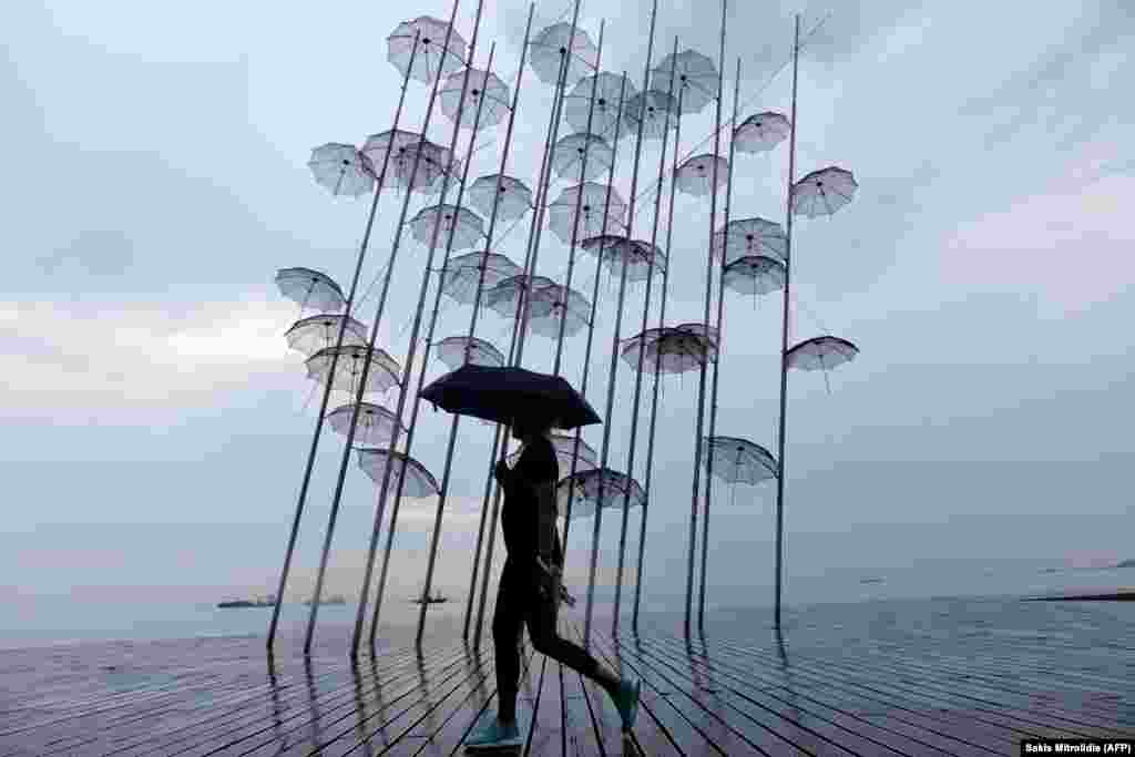 A woman with an umbrella walks past a sculpture called Umbrellas by Greek sculptor George Zongolopoulos, along the waterfront in Thessaloniki. (AFP/Sakis Mitrolidis)