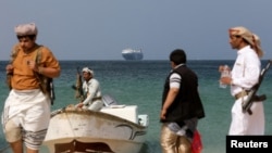 گروهی از مردان مسلح حوثی‌ مسلح در ساحل؛ در نمای دورتر کشتی تجاری گلکسی لیدر دیده می‌شود که توسط آن‌ها توقیف شده است