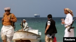 Armed men stand on the beach as the Galaxy Leader commercial ship, seized by Yemen's Huthis in November, is anchored off the coast of Salif.