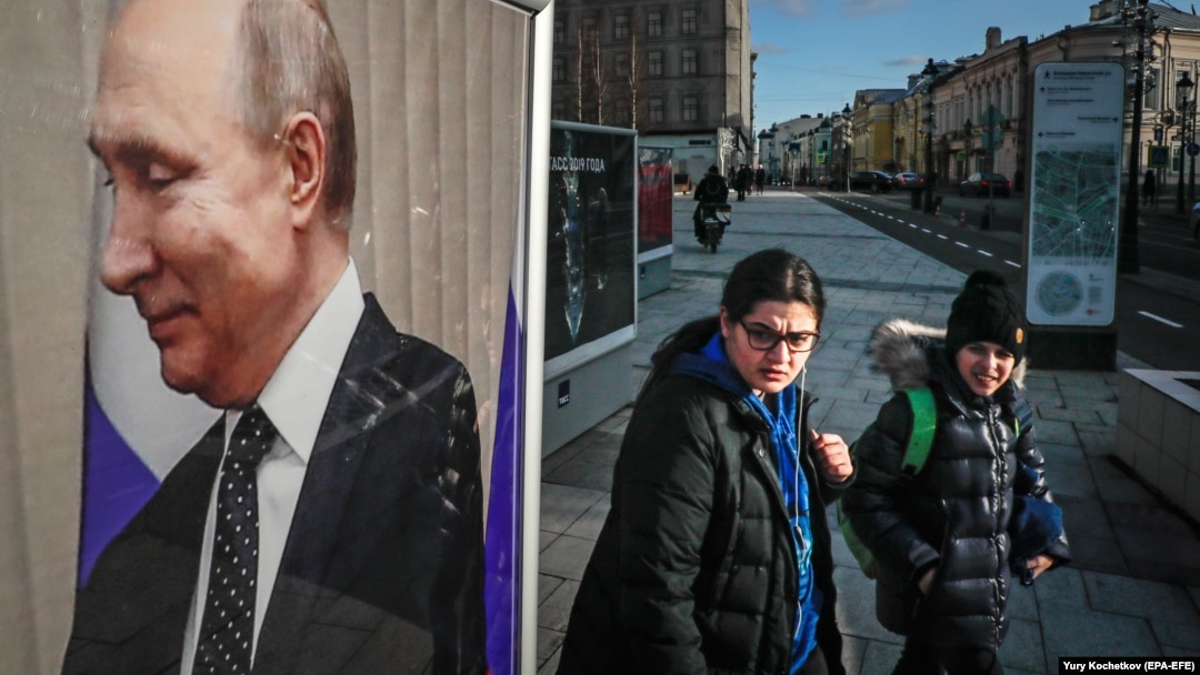 Russians walk near a large photograph of Russian President Vladimir Putin in the center of Moscow.