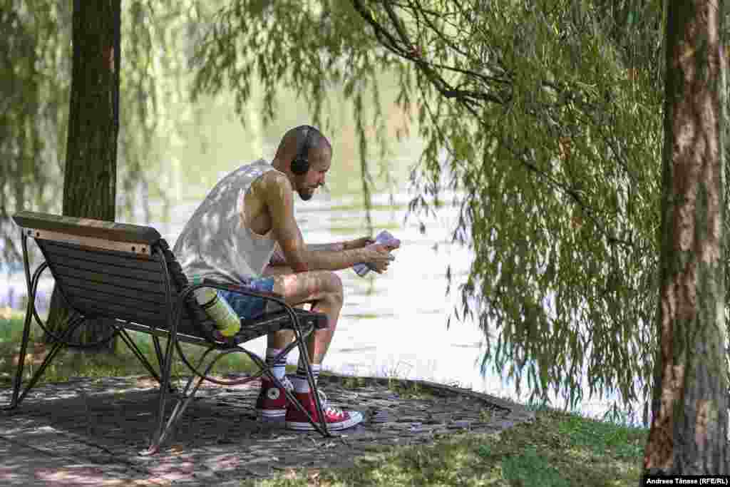 Un bărbat citește o carte lângă lacul din parcul IOR din București.