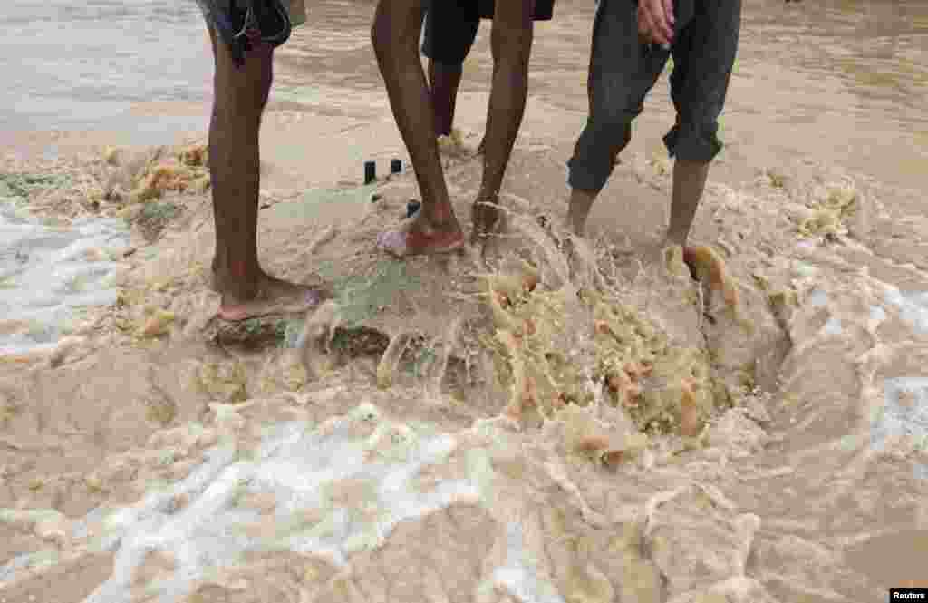 Barefooted men take a break on a road median while wading through floodwaters on the outskirts of Karachi.