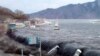 On top, an image taken by a Miyako city official on March 11, 2011, of the tsunami breeching an embankment and flowing into the city of Miyako in Iwate Prefecture, and below, the same area on January 16, 2012