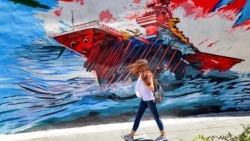 A woman in Tehran walks past an anti-US and anti-Israel mural depicting missiles hitting an aircraft carrier. 