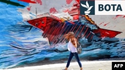 Një grua iraniane kalon pranë një murali antiamerikan dhe antiizraelit ku shfaqen raketat iraniane duke goditur një aeroplanmbajtëse. Teheran, 26 maj 2026. 