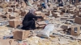 یک زن فلسطینی در حال جست‌وجو در کارتن‌های «بنیاد بشردوستانه غزه» (جی‌اچ‌اف)؛ رفح، پنجشنبه ۱۵ خرداد