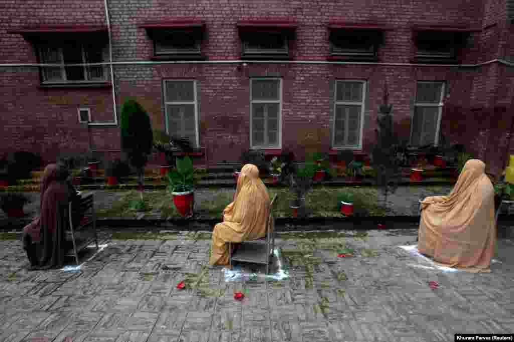 Burqa-clad women in Peshawar, Pakistan, sit on chairs maintaining a safe distance as they wait for their turn to receive emergency aid as part of a program introduced by the government for vulnerable families due to the spread of the coronavirus. (Reuters/Khuram Parvez)