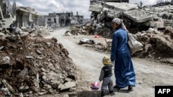 A Kurdish Syrian woman walks with her child past the ruins of Kobani after Islamic State militants had been pushed out of the town earlier this year. 