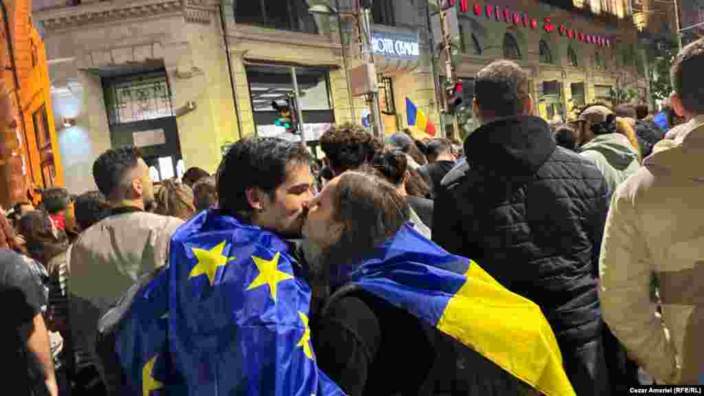 Doi tineri fericiți se sărută, după ce rezultatele exit-poll-urilor și rezultatele oficiale parțiale au indicat victoria democratului Nicușor Dan în alegerile prezidențiale din România, cu alte cuvinte menținerea direcției euroatlantice a țării.Mii de simpatizanții primarului Bucureștiului s-au adunat în fața unei clădiri istorice din apropierea sediului vechi al Primăriei Capitalei, pe Bulevardul Elisabeta, ca să celebreze victoria.