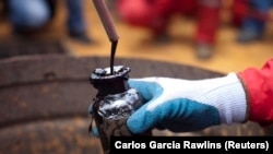 Работник собира примерок од сурова нафта на нафтен бунар управуван од државната нафтена компанија на Венецуела