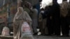 A woman, clad in burqa, carries a sack of flour, purchased from a truck along a road in the northwestern city of Peshawar on January 20.