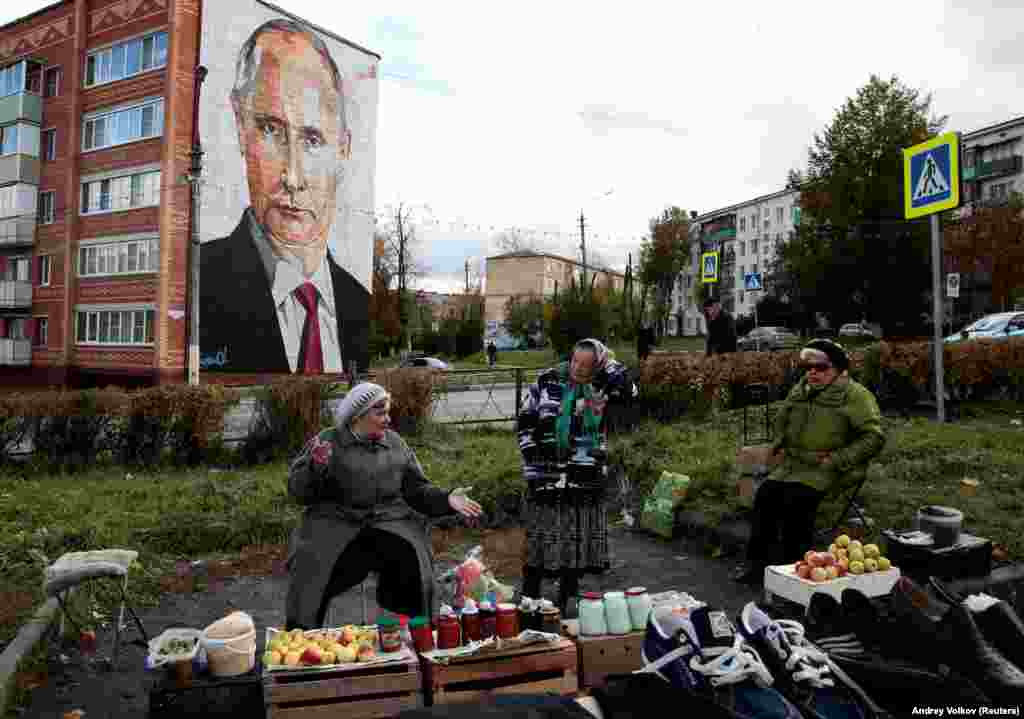 Moskwanyň daşyndaky Kaşira şäherinde aýallar köçe bazarynda azyk satýarlar. Arkada prezident W.Putiniň portreti görünýär. (Reuters/Andrey Volkov)